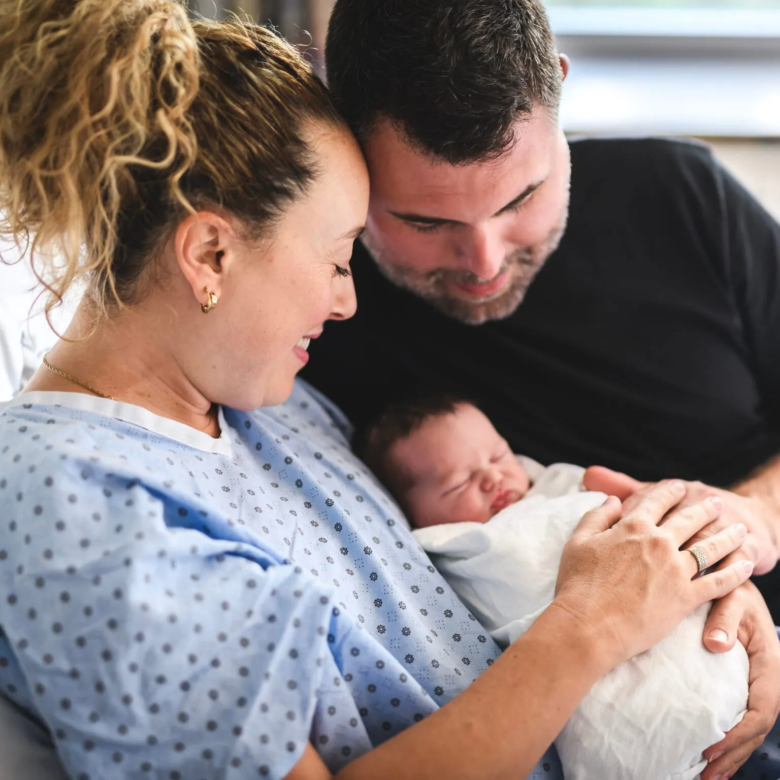 New parents in a hospital bed smiling at their newborn baby