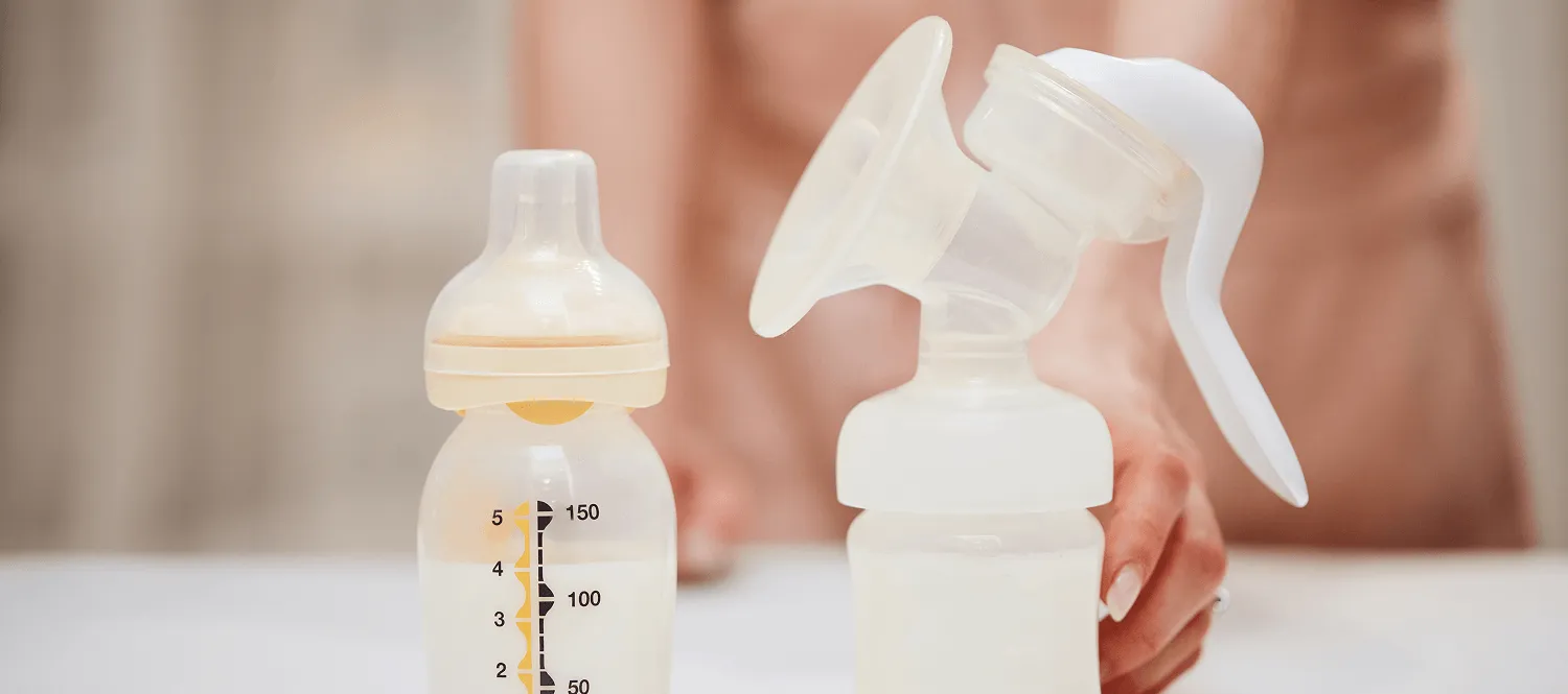 Bottles of pumped breast milk beside a manual breast pump